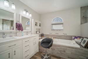 Full bath with double vanity, wood finished floors, a garden tub, and a sink