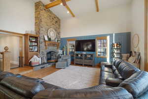 Living area with wood finished floors, baseboards, high vaulted ceiling, a fireplace, and beamed ceiling