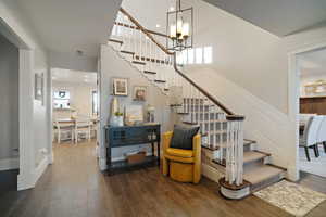 Staircase with a high ceiling, an inviting chandelier, wood finished floors, and a decorative wall