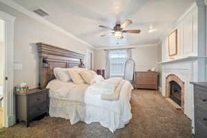 Bedroom with visible vents, carpet, a brick fireplace, and ornamental molding