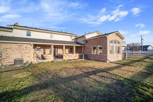 Rear view of house featuring a patio, central AC unit, a lawn, and brick siding