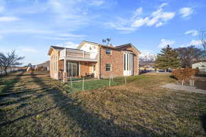 Back of house with brick siding, a lawn, and a balcony