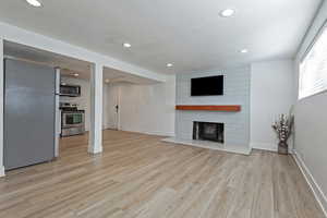 Unfurnished living room with recessed lighting, light wood-type flooring, a large fireplace, and baseboards