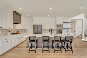 Kitchen with white cabinets, appliances with stainless steel finishes, light wood-style floors, and a kitchen island with sink