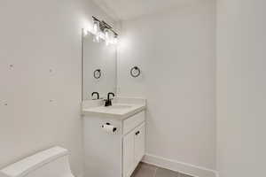 Half bath featuring tile patterned flooring, toilet, vanity, and baseboards