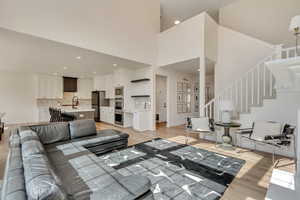 Living area featuring baseboards, stairway, light wood-type flooring, recessed lighting, and a high ceiling