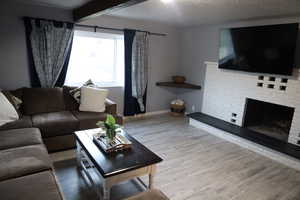 Living area with a textured ceiling, a fireplace, wood finished floors, baseboards, and beam ceiling