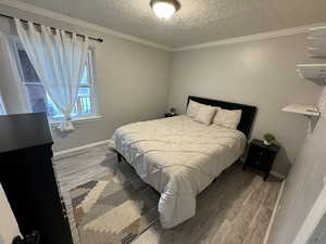 Bedroom featuring crown molding, a textured ceiling, baseboards, and wood finished floors