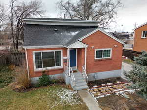 Bungalow-style house featuring brick siding, roof with shingles, and fence