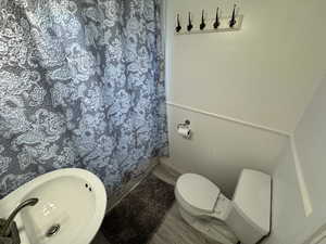 Full bath featuring curtained shower, toilet, wainscoting, a sink, and wood finished floors
