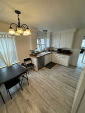 Kitchen with pendant lighting, stainless steel dishwasher, light wood-style floors, white cabinets, and a sink