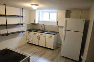 Kitchen featuring white appliances, light wood finished floors, a sink, decorative backsplash, and dark countertops