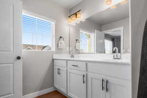 Full bathroom featuring double vanity, wood finished floors, baseboards, and a sink
