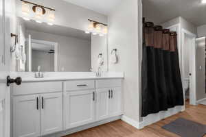 Bathroom with a shower with shower curtain, wood finished floors, baseboards, double vanity, and a sink