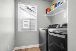 Clothes washing area with washer and clothes dryer, laundry area, baseboards, and wood finished floors