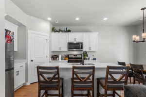 Kitchen with light wood-style flooring, a sink, stainless steel appliances, light countertops, and a kitchen breakfast bar