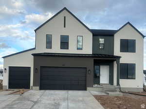 View of front facade with a standing seam roof, an attached garage, driveway, and metal roof