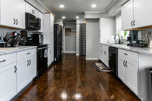 Kitchen with black appliances, a sink, light stone counters, crown molding, and dark wood-style flooring
