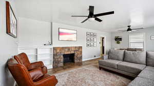 Living room featuring a stone fireplace, wood finished floors, baseboards, and a ceiling fan