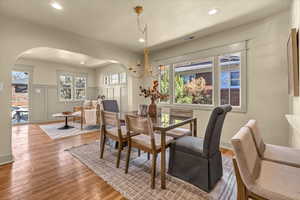 Dining space featuring wood finished floors, visible vents, arched walkways, wainscoting, and a decorative wall