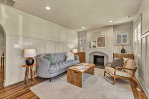 Living room featuring visible vents, a fireplace with flush hearth, wood finished floors, arched walkways, and a decorative wall