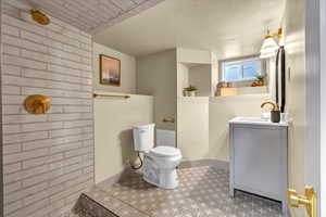 Full bath with toilet, a textured ceiling, a tile shower, baseboards, and vanity