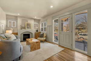 Living room with a fireplace with flush hearth, a wainscoted wall, recessed lighting, wood finished floors, and a decorative wall