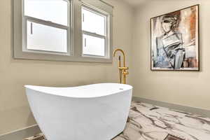 Bathroom featuring marble finish floor, baseboards, and a freestanding tub