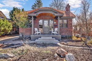 View of front of home featuring a tile roof, covered porch, brick siding, and a chimney