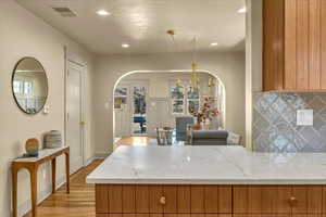 Kitchen featuring brown cabinetry, visible vents, wood finished floors, arched walkways, and tasteful backsplash