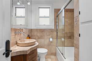 Bathroom featuring enclosed tub / shower combo, toilet, tile walls, and vanity