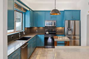 Kitchen featuring pendant lighting, decorative backsplash, stainless steel appliances, blue cabinets, and a sink