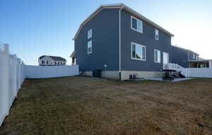 Rear view of house featuring a patio area, central air condition unit, a lawn, and a fenced backyard
