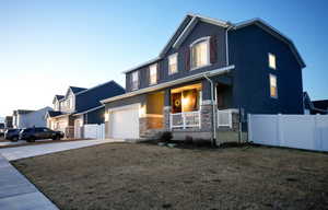 View of front of property featuring fence, a porch, concrete driveway, stucco siding, and stone siding