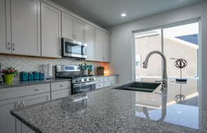Kitchen with a sink, stone countertops, backsplash, and appliances with stainless steel finishes