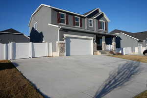 View of front facade with stucco siding, a gate, stone siding, concrete driveway, and a garage