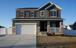 Craftsman inspired home featuring stone siding, a porch, an attached garage, and fence