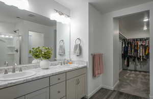 Full bathroom with double vanity, a stall shower, a spacious closet, and a sink