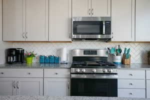 Kitchen featuring decorative backsplash, light stone countertops, appliances with stainless steel finishes, and white cabinets