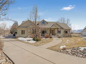 View of front of house with stone siding, covered porch, a shingled roof, and fence