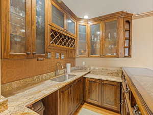 Kitchen with light stone counters, light wood-type flooring, glass insert cabinets, and a sink