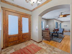 Entrance foyer featuring ornamental molding, ceiling fan with notable chandelier, french doors, arched walkways, and baseboards