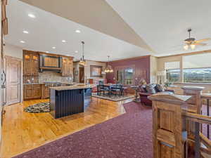 Kitchen with a breakfast bar area, an island with sink, decorative backsplash, brown cabinets, and exhaust hood