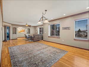 Living area featuring light wood-type flooring, arched walkways, baseboards, and crown molding