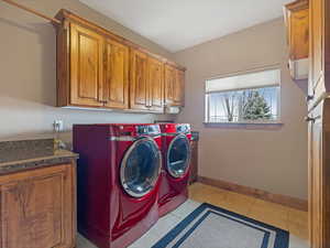 Clothes washing area featuring washer and dryer, baseboards, cabinet space, and light tile patterned floors