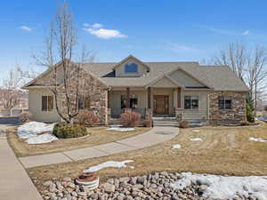 View of front of home featuring stone siding, roof with shingles, and covered porch