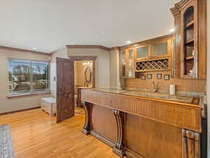 Bar with crown molding, baseboards, indoor wet bar, decorative backsplash, and light wood-style flooring