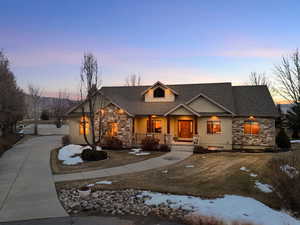 View of front of property with stone siding, roof with shingles, a porch, and driveway