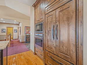 Kitchen with light wood finished floors, oven, built in microwave, lofted ceiling, and arched walkways