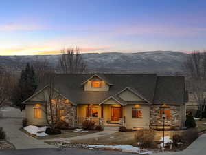 View of front facade with a mountain view, stone siding, a porch, and fence